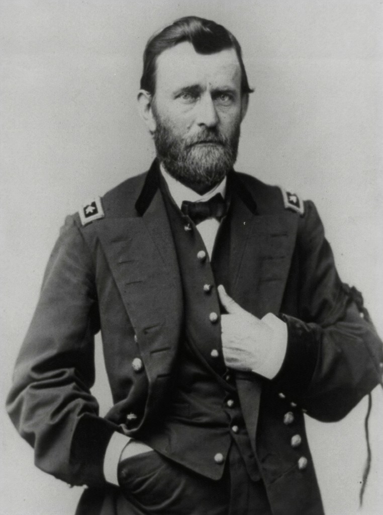 A black-and white photo of a white man in a dark suit with stars on the shoulders that appears just a little too big. The bow-tie is crooked. The man's hair is dark, although his short, neat beard is starting to go gray. His eyes are light, and he looking directly at the camera with a subtle but definite expression of sadness and fear. In fact, it is a formal photo of U.S. Grant, taken when he was in his early forties. The photo looks slightly narrow, as though it has been squeezed. I don't know whether it has been.